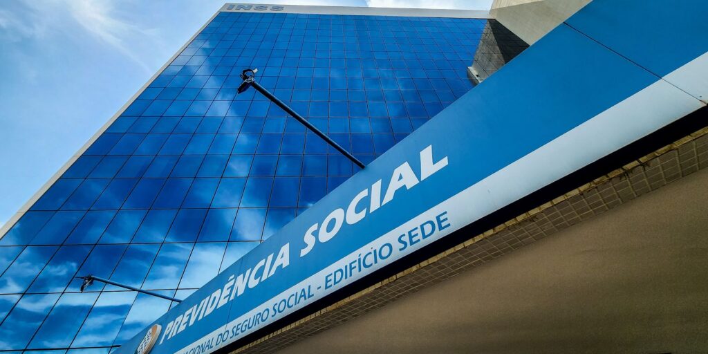 Fachada espelhada do prédio-sede do INSS em Brasília, com a placa azul "Previdência Social - Edifício Sede"